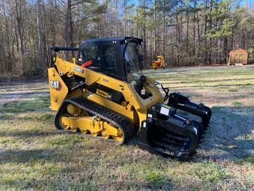 A bulldozer with a grapple attached to it is parked in a grassy field.