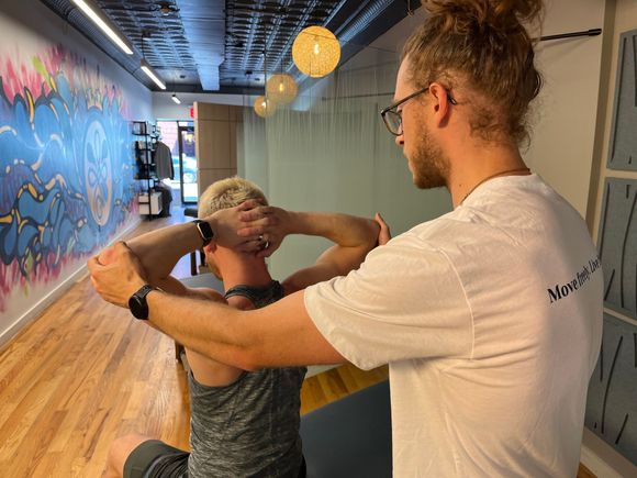 A man is stretching another man 's neck in a gym.