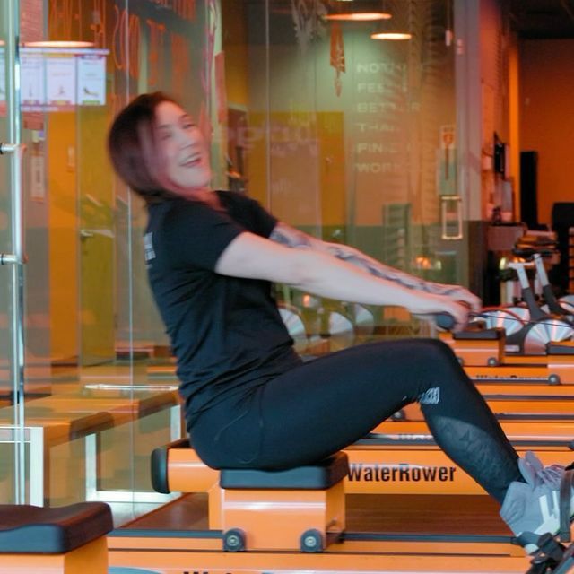 A woman is sitting on a waterrower in a gym
