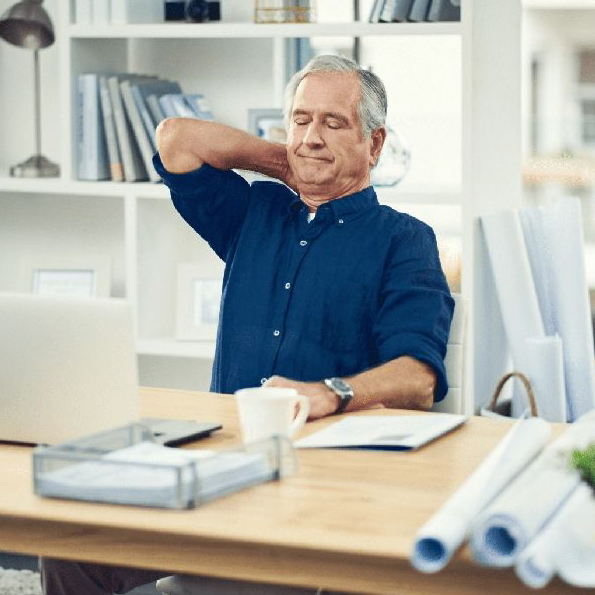 A man in a blue shirt is sitting at a desk with his hands behind his head.