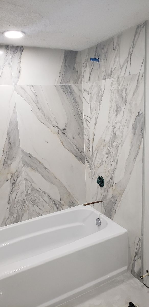 A bathroom with a bathtub , shower , and marble wall.