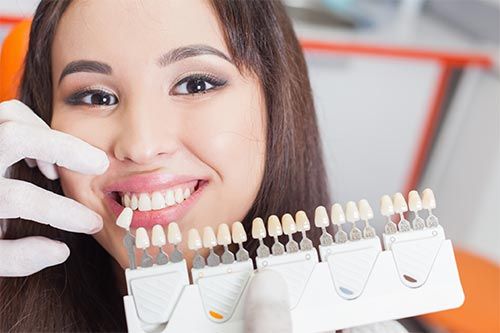 a woman is smiling while holding a tooth color chart in front of her teeth .