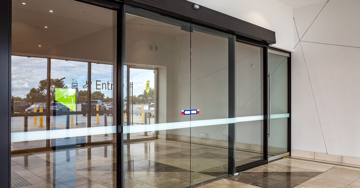 Automatic sliding doors made of glass at the front of a building. The word entrance is etched into t