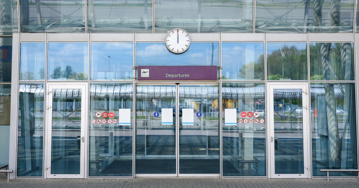 Automatic sliding glass doors at the entrance of an airport. Above the doors are an analog clock.