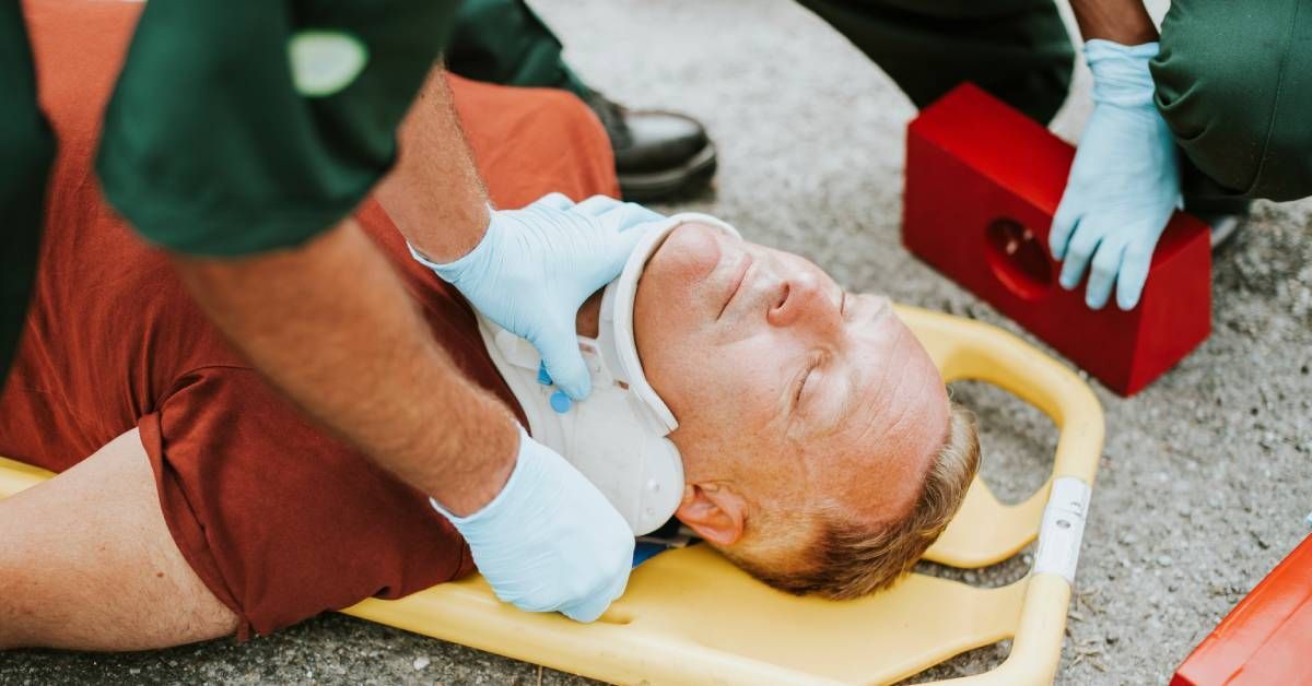 An injured man lying on a yellow stretcher while medical personnel attach a cervical collar around h