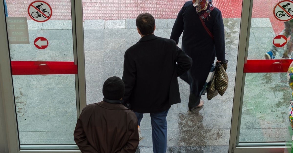 Three people—a woman and two men—walking out of a building through a sliding glass door and onto the