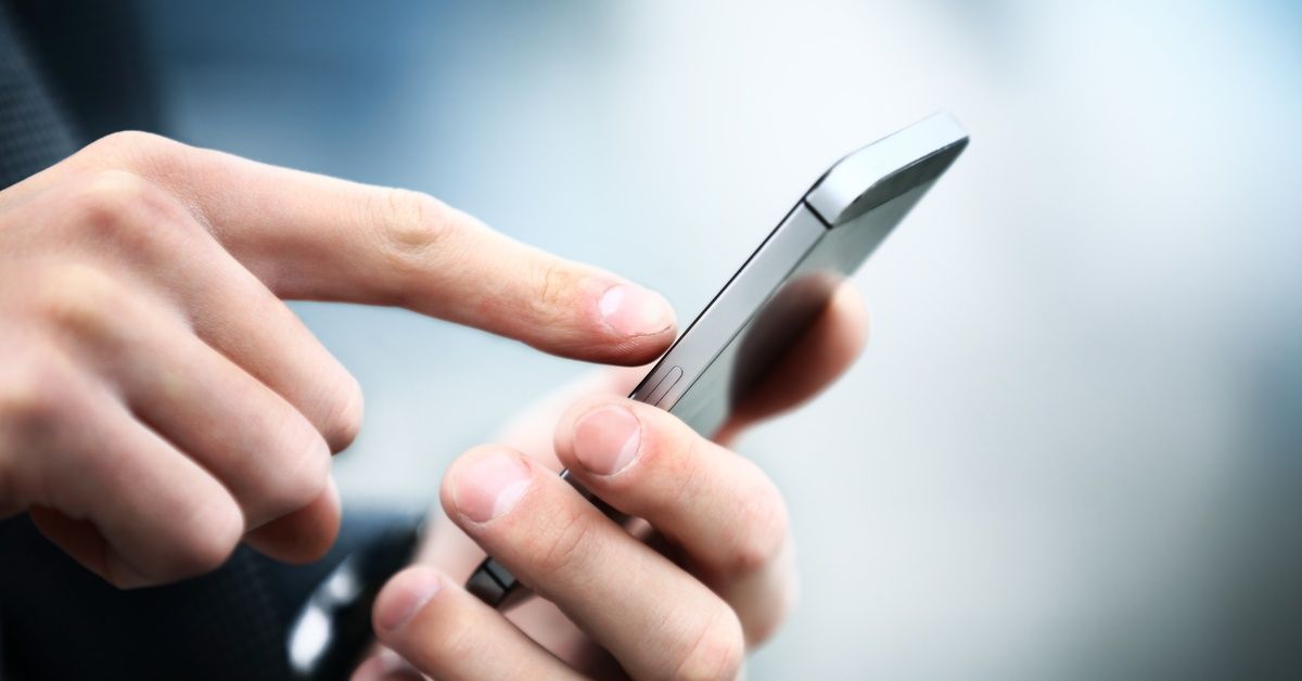 A close-up of a person's hands. They're holding a smartphone in their left hand and tapping the scre