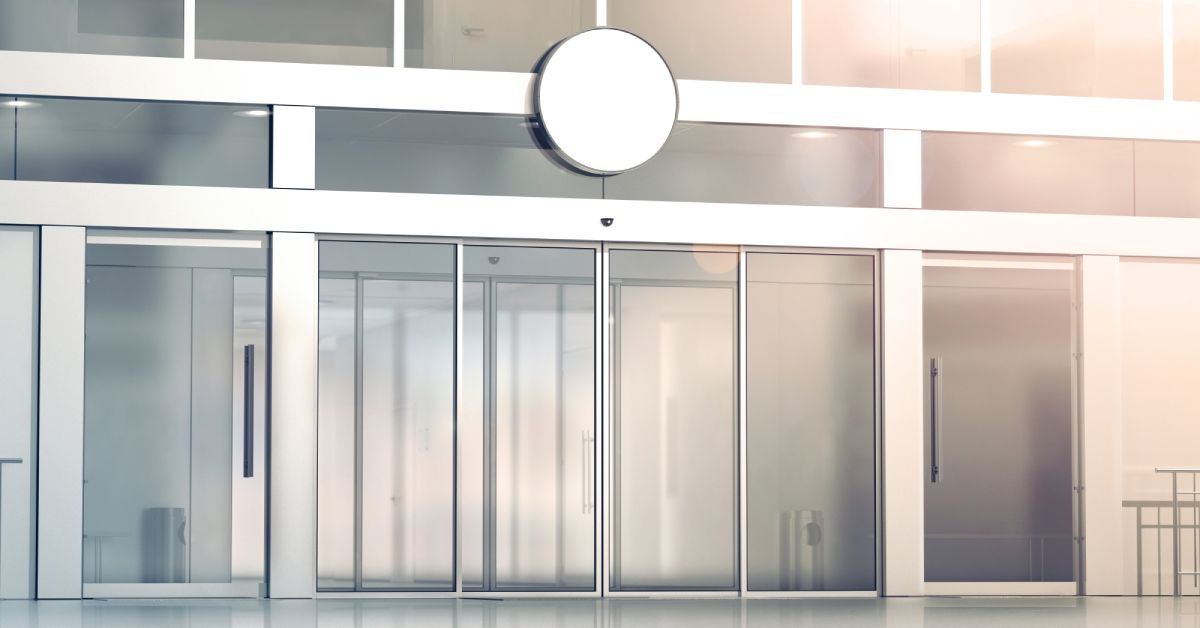 Modern commercial sliding doors made of glass with sleek white frames. White walls and floors surrou