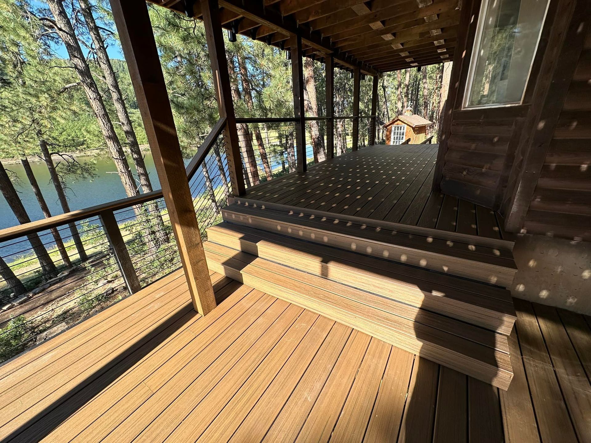 Wooden deck with stairs leading to a shaded porch; overlooking a lake and trees.