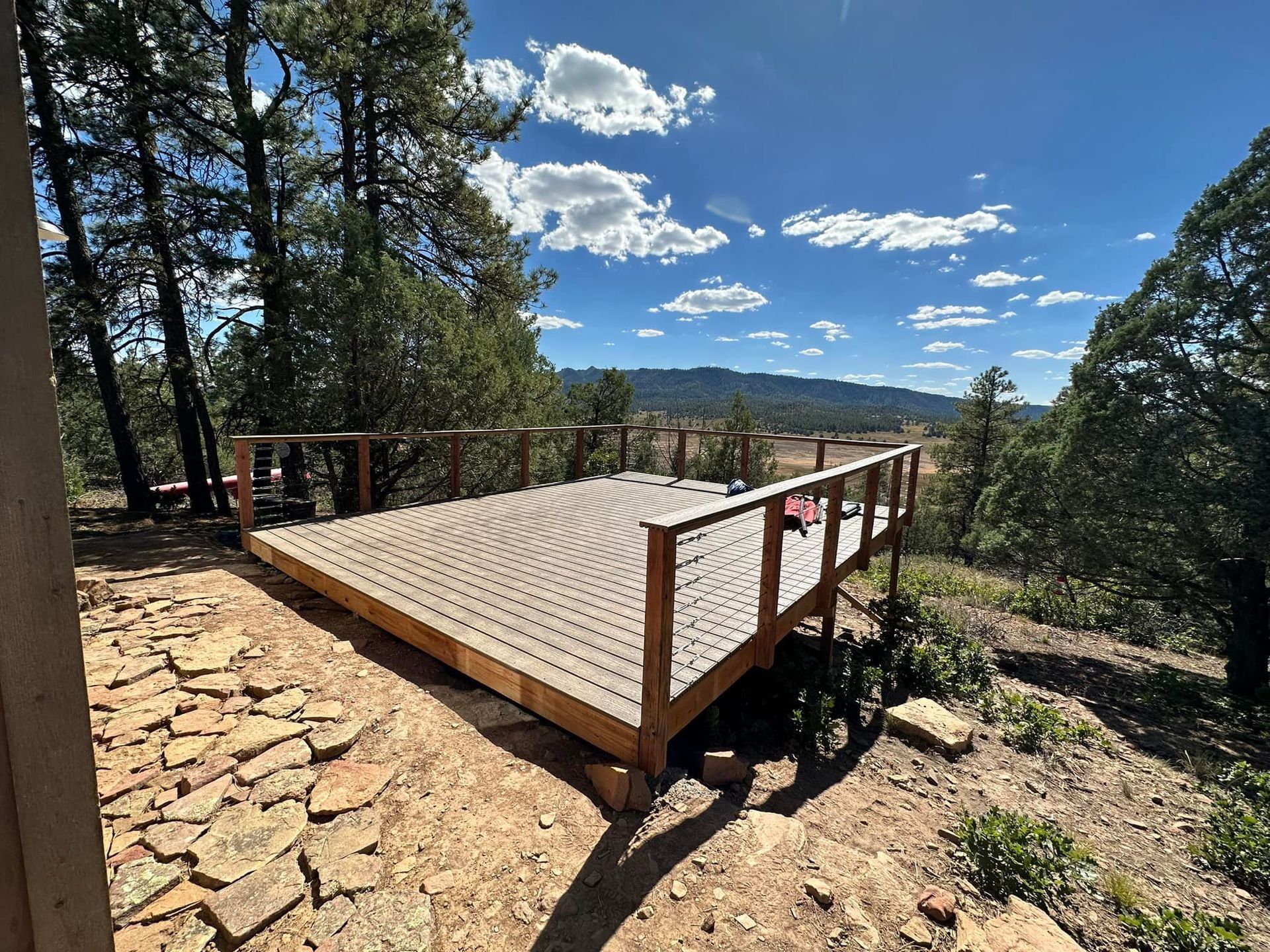 Wooden deck with railing, overlooking a scenic view of a landscape under a blue sky.