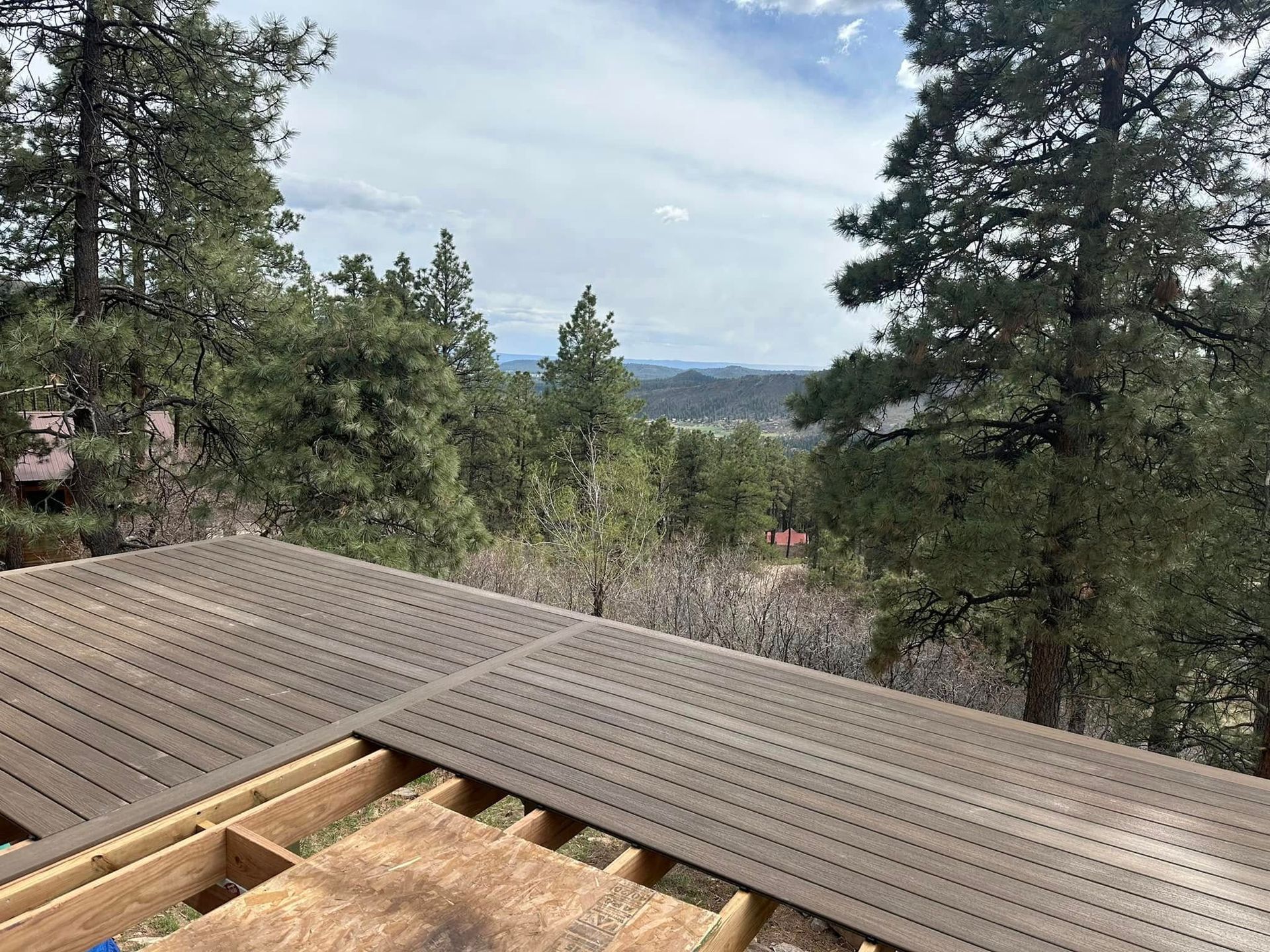 View from a deck overlooking a forest and distant town under a cloudy sky.