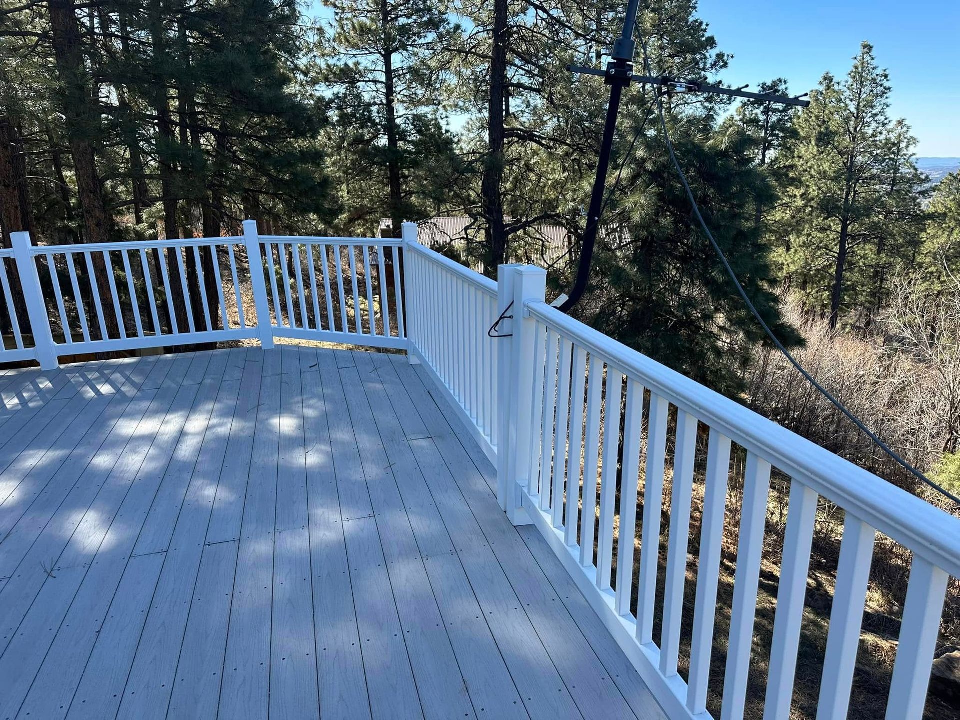 White deck with railing overlooking a forest, clear blue sky above.