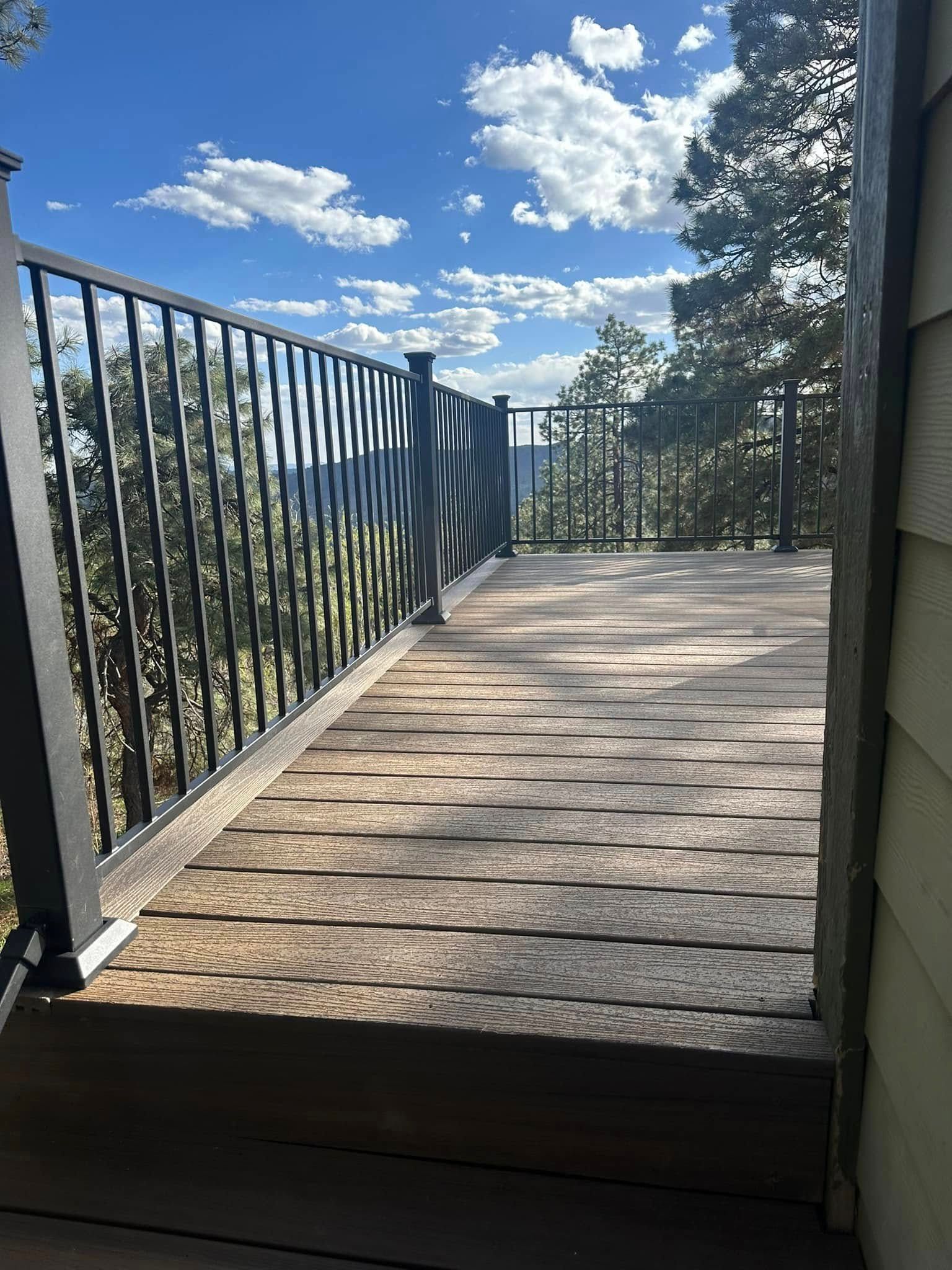 Deck with black railing overlooks a mountainous landscape under a blue sky with fluffy clouds.