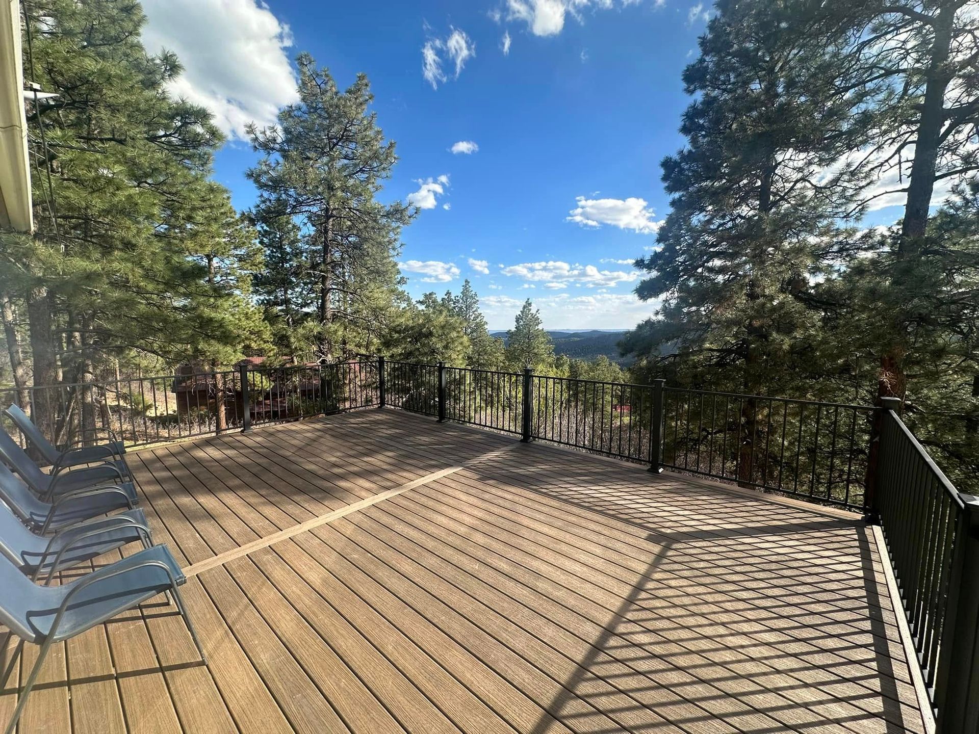 Wooden deck surrounded by pine trees, overlooking a scenic mountain view under a blue sky.