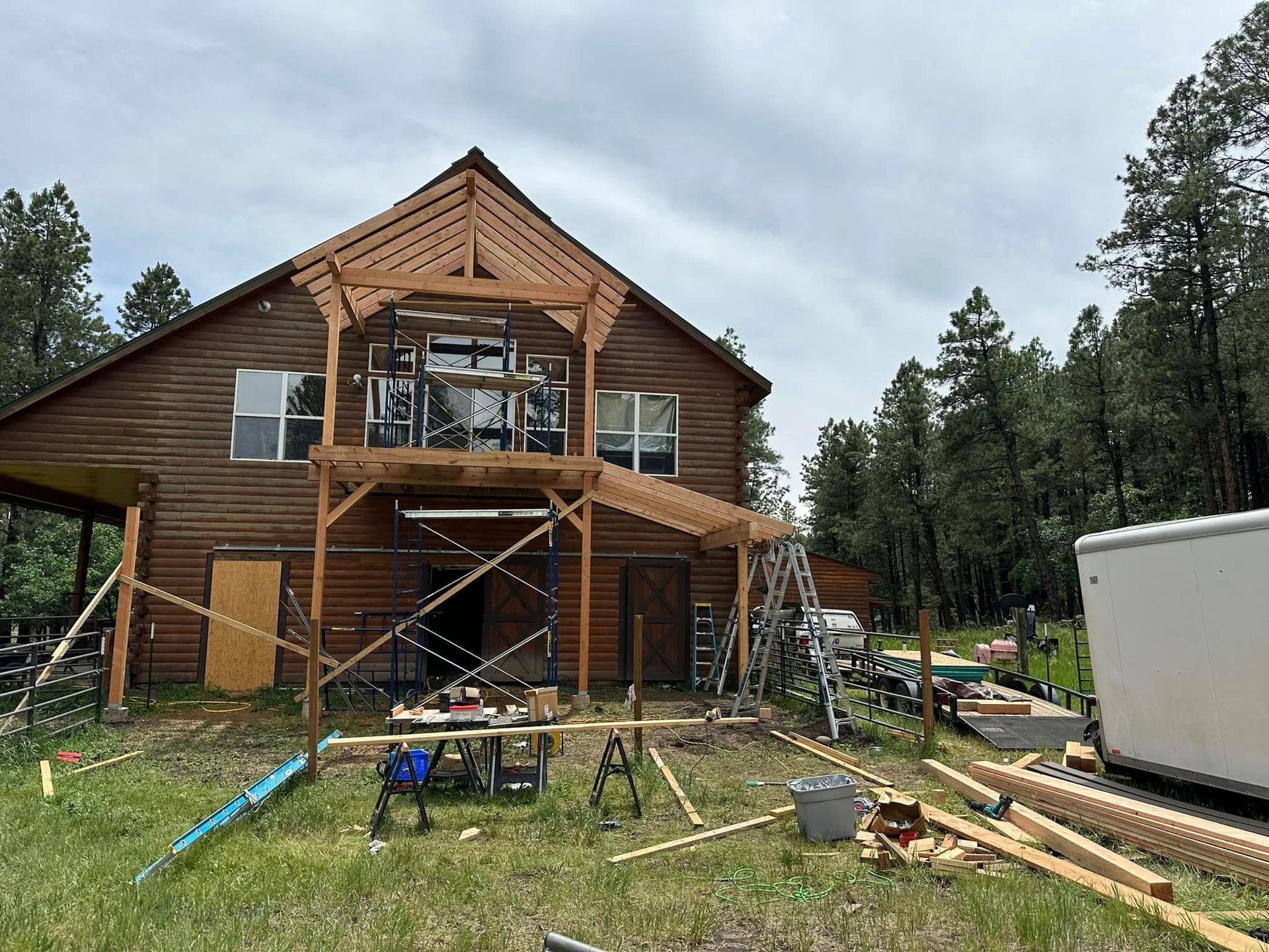 Barn under construction with scaffolding and lumber in a grassy area surrounded by trees.