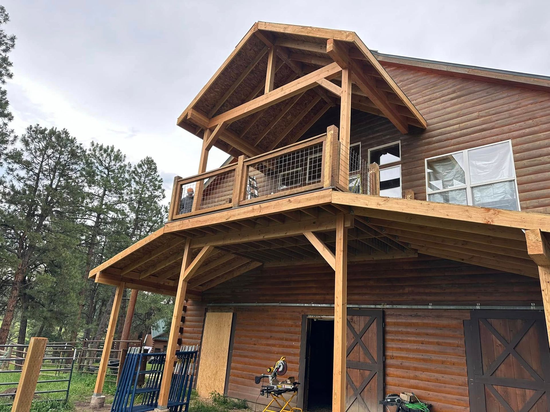 Log cabin with wooden deck and balcony under construction, set against a cloudy sky.