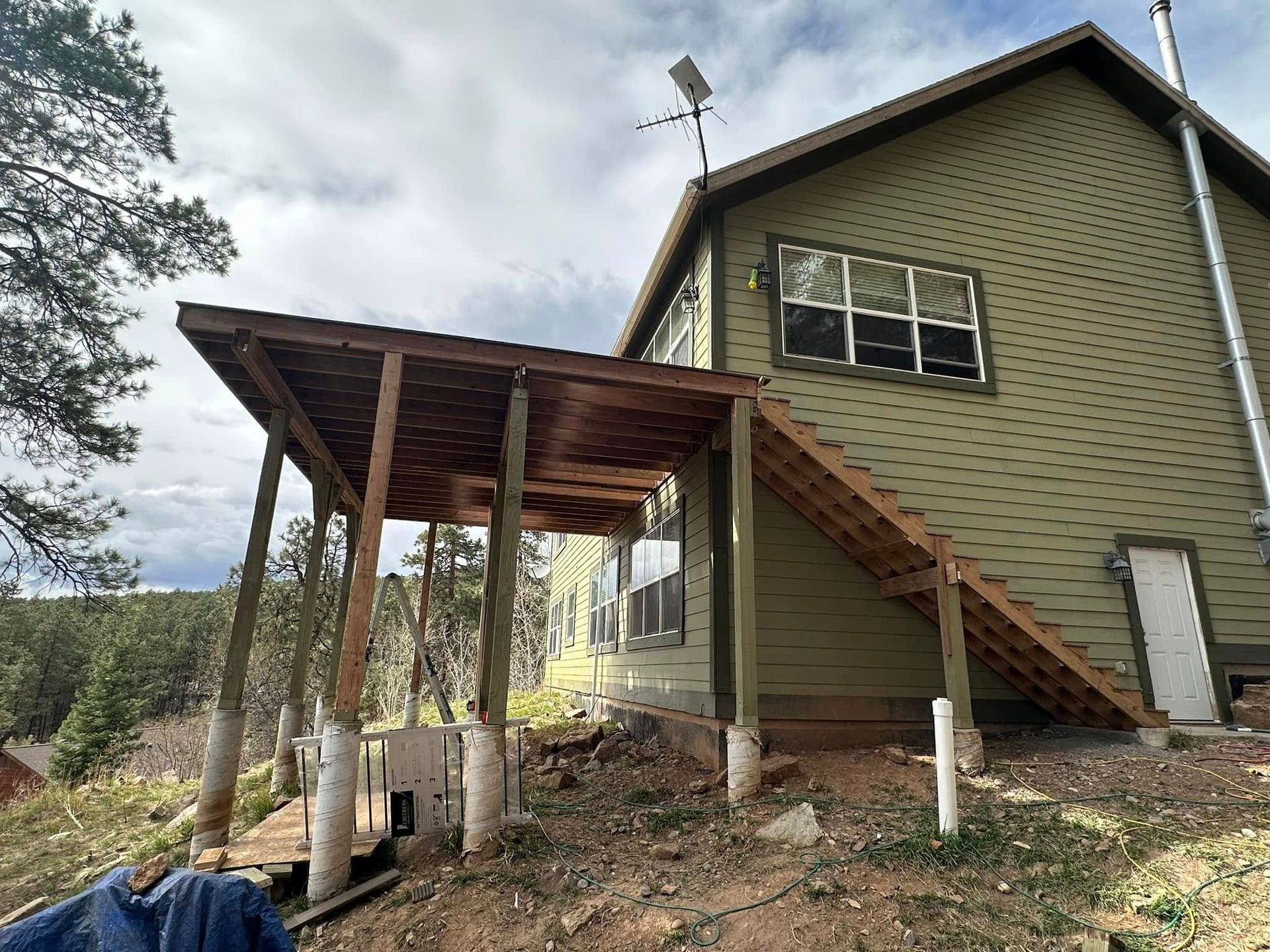 Green house with wooden porch and stairs; set in a natural, slightly hilly landscape.