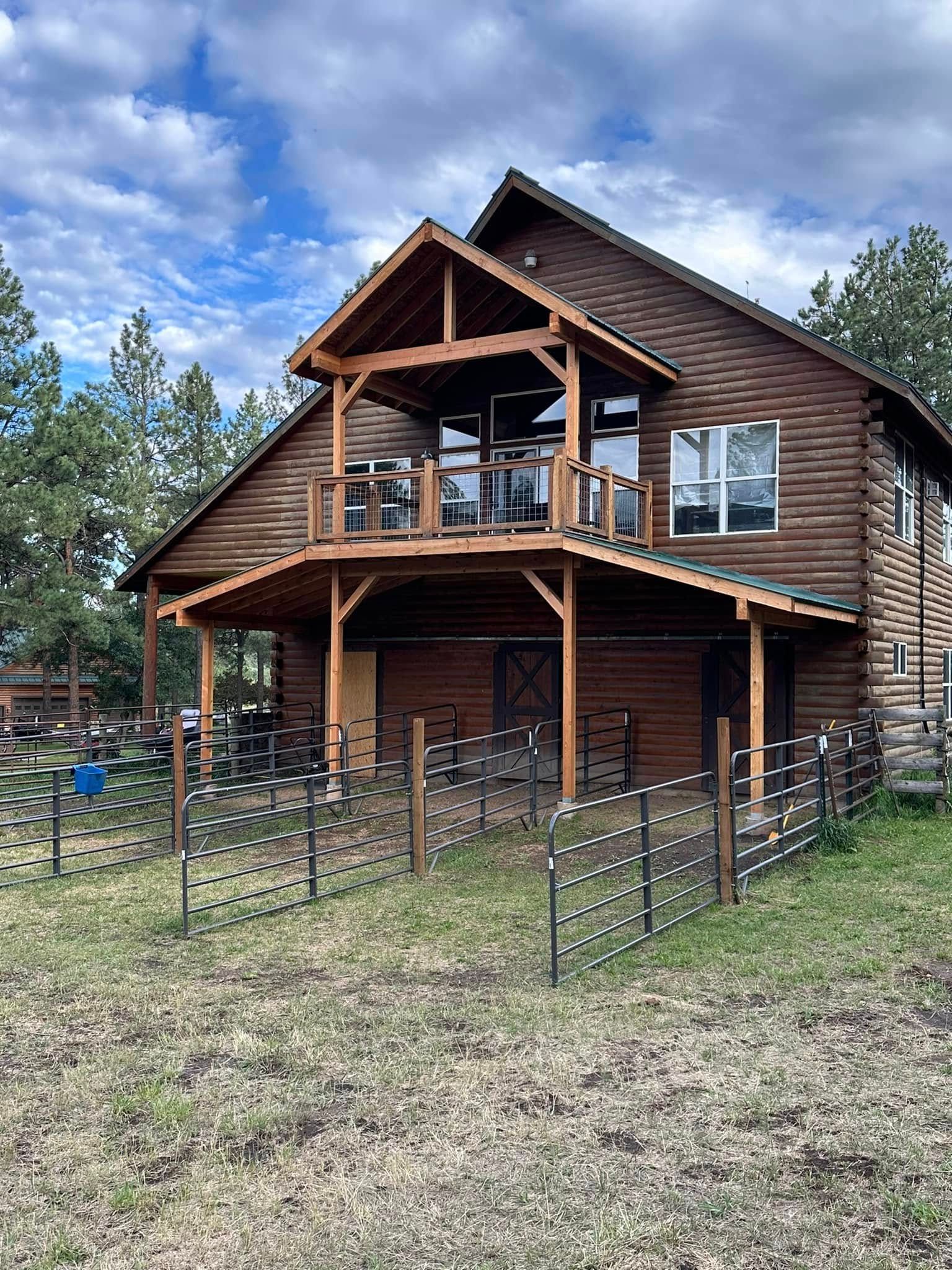 Rustic cabin with a balcony and fenced yard, set against a cloudy sky.