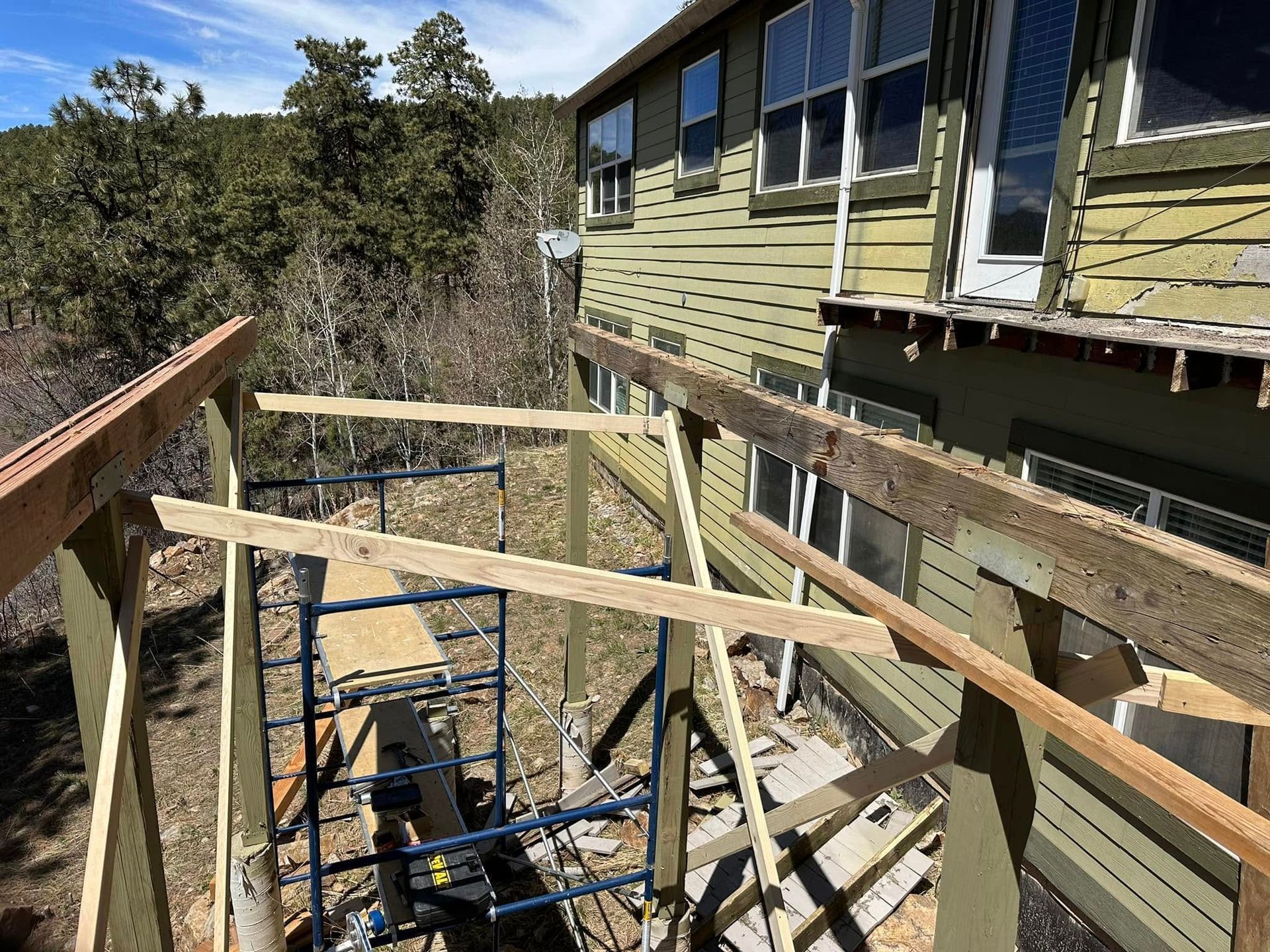 Construction of a wooden structure next to a green house on a hillside, scaffolding visible.