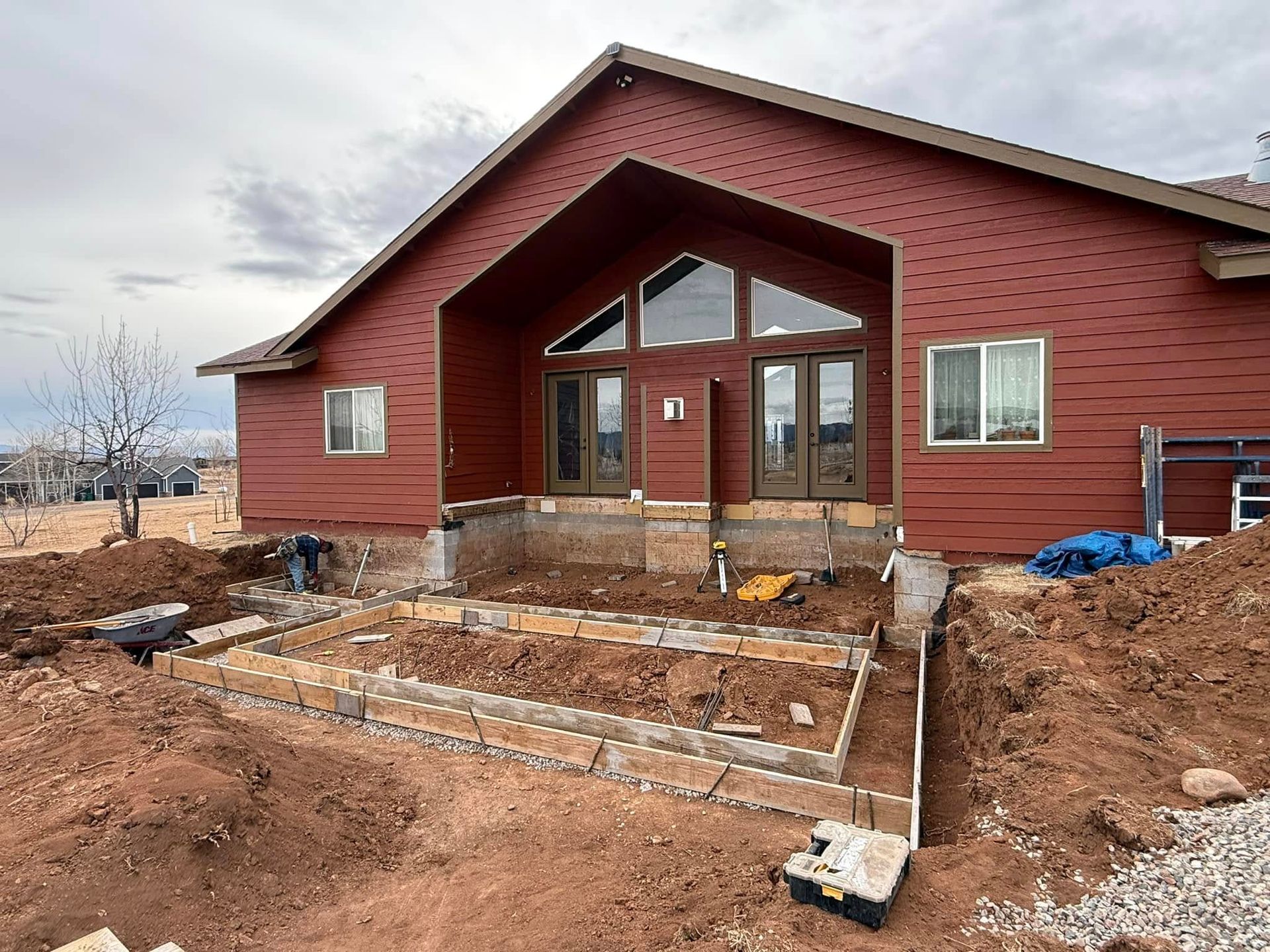 Exterior home renovation: digging around a red-sided house. New retaining wall is being built, soil piled around.