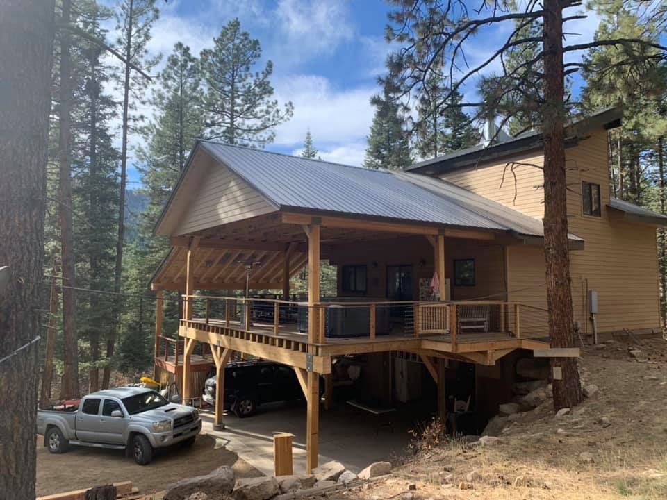 Wooden cabin with porch and metal roof, set in a forest. A truck is parked in the driveway.
