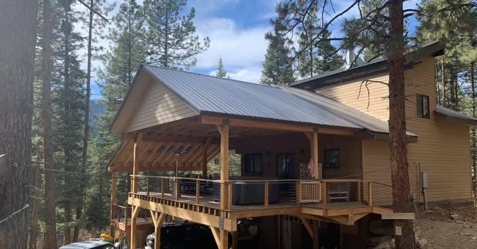 Cabin in a forest setting with wooden deck and metal roof.