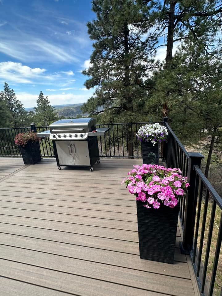 Deck with grill, flowerpots, and scenic mountain views under a bright blue sky.