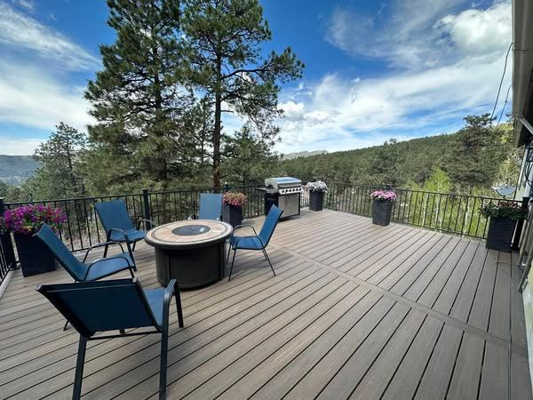 Deck with seating and grill overlooking a forested valley under a blue sky.