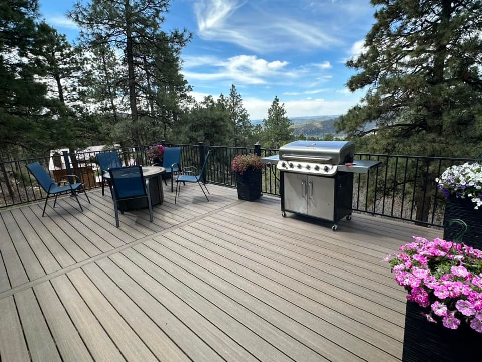 Composite deck with grill, table, chairs, potted flowers, and trees with a scenic view.