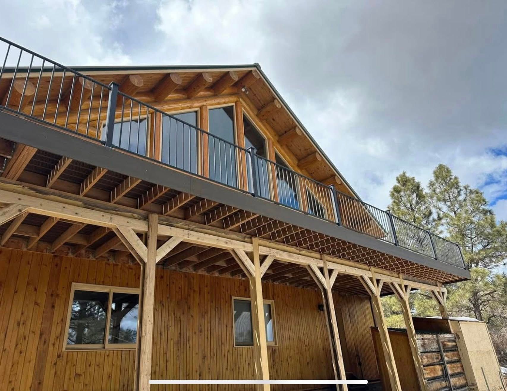 Wooden house with upper balcony and black railing under cloudy sky.