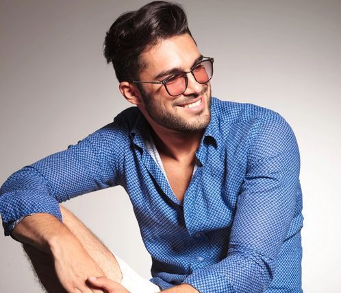 A man wearing sunglasses and a blue shirt is sitting down and smiling.