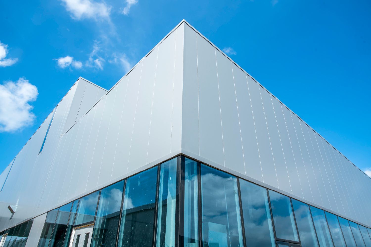 Modern building with metallic siding and large glass windows against a blue sky.