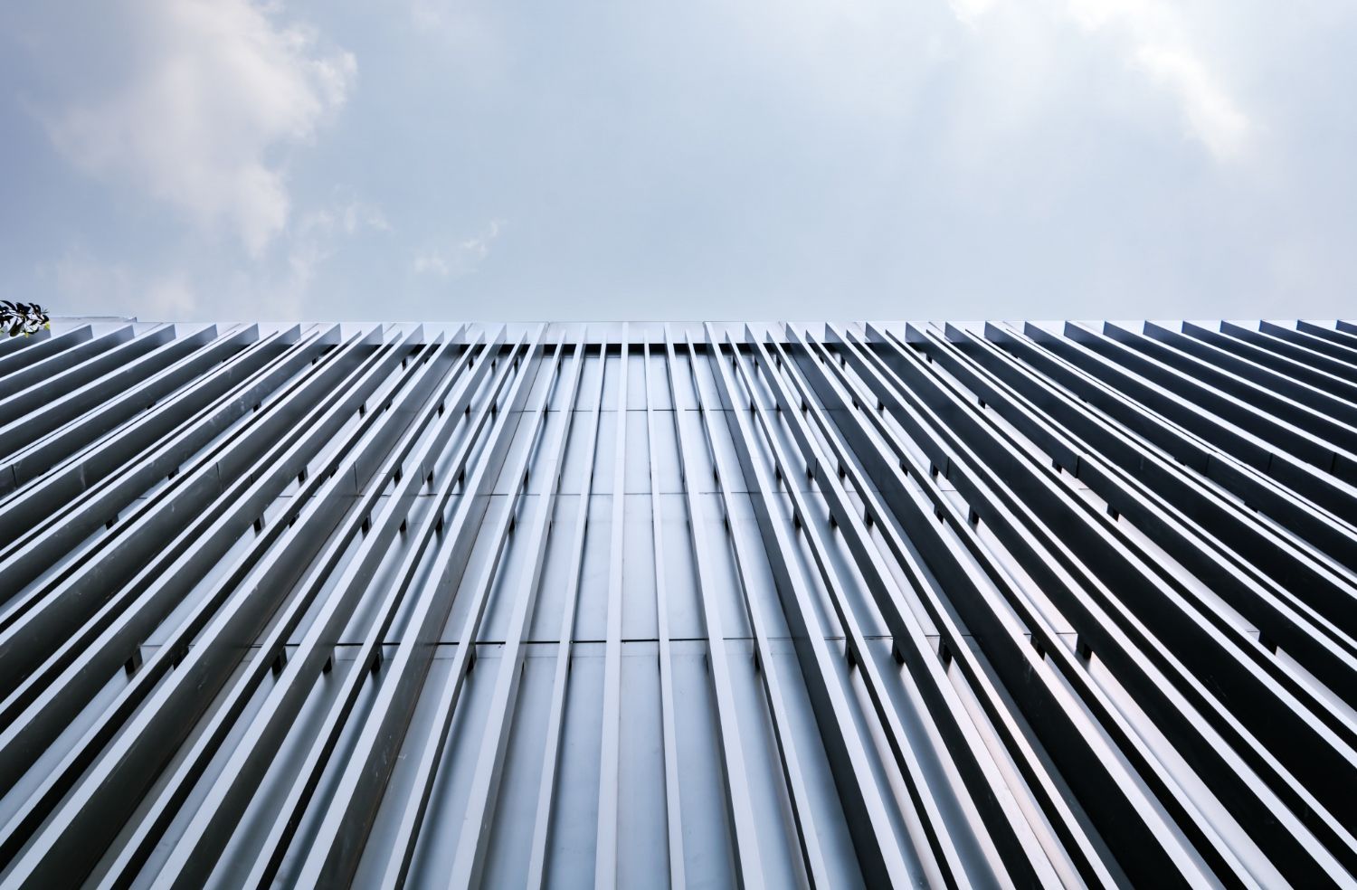 Low-angle view of a building with vertical, silver, ridged facade, beneath a pale blue sky.
