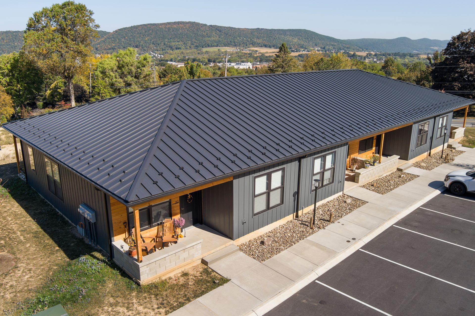 Aerial view of a single-story dark grey building with a metal roof and front porches, located next to a paved parking lot.