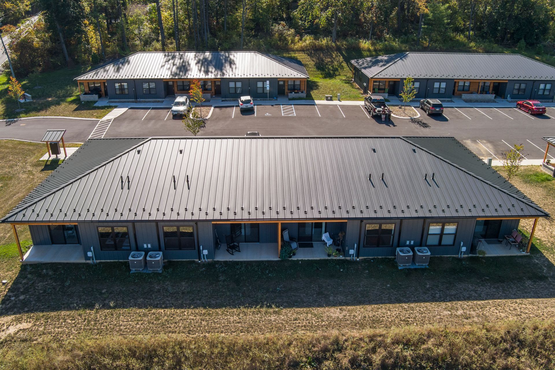 Aerial view of three modern, gray, single-story apartment buildings with black metal roofs and adjacent parking lots.