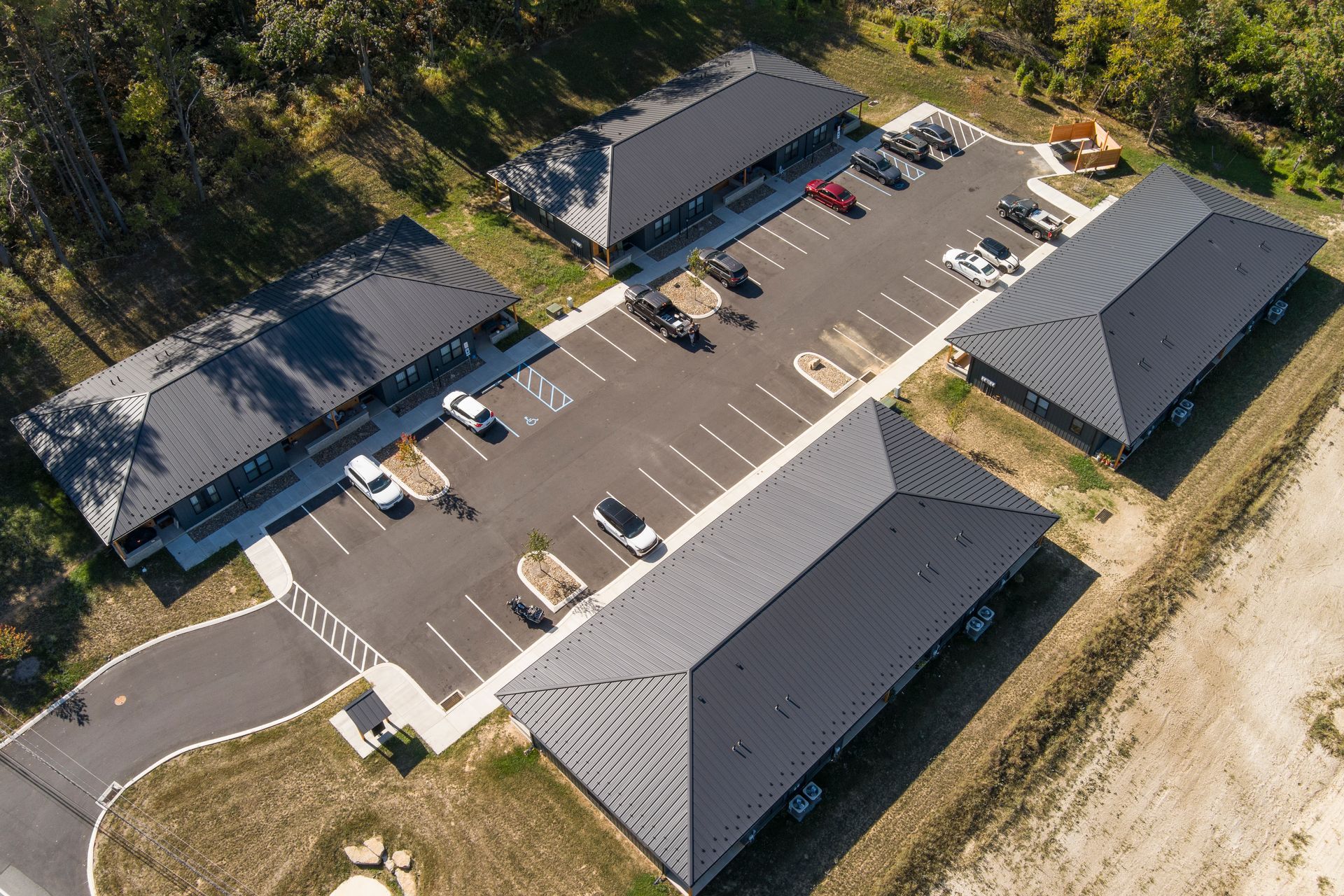 An aerial view of four dark metal-roofed commercial buildings arranged in a square around a central paved parking lot.