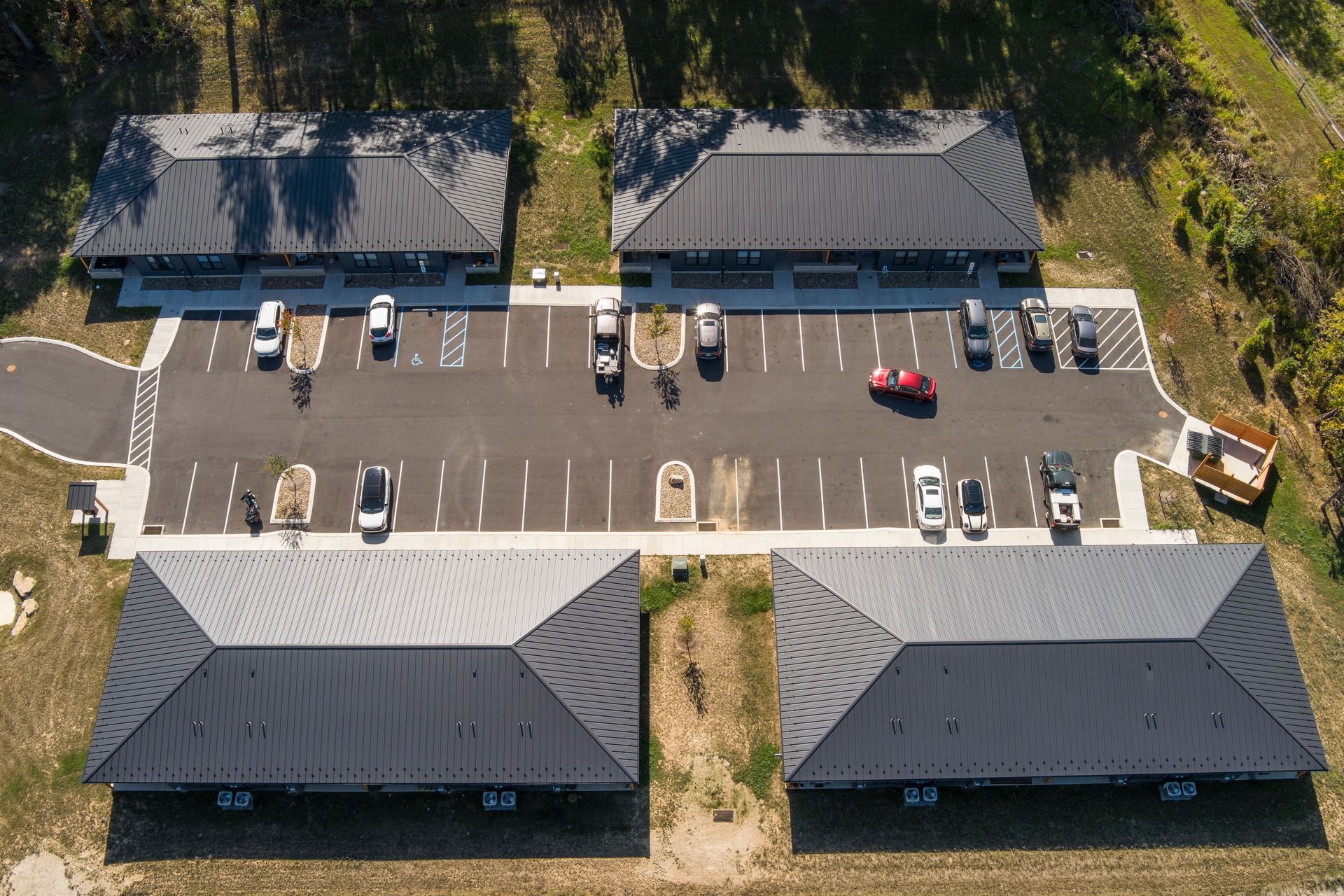 Aerial view of four gray metal-roofed buildings arranged in a square around a central parking lot with several parked cars.