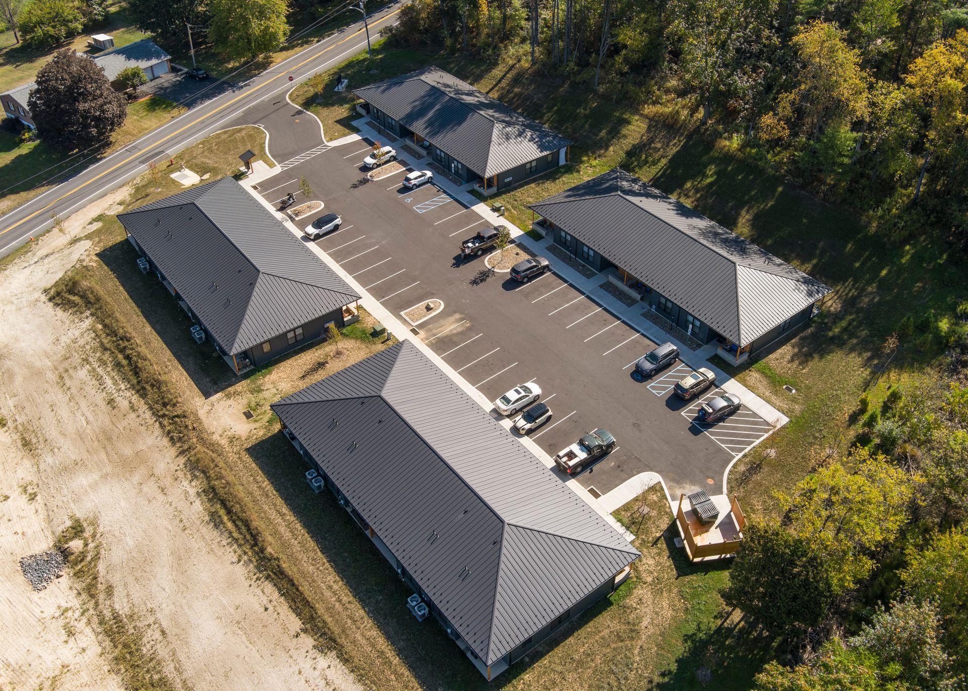 Aerial view of a complex with three dark metal-roofed buildings arranged around a parking lot