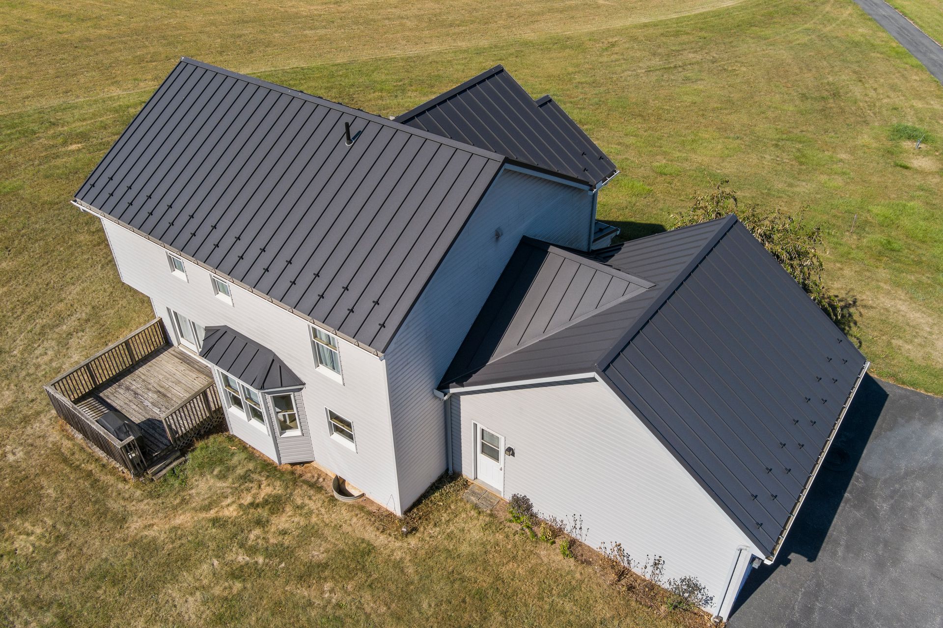 An aerial view of a two-story house with a black metal roof, light siding, and an attached garage set on a grassy lawn.