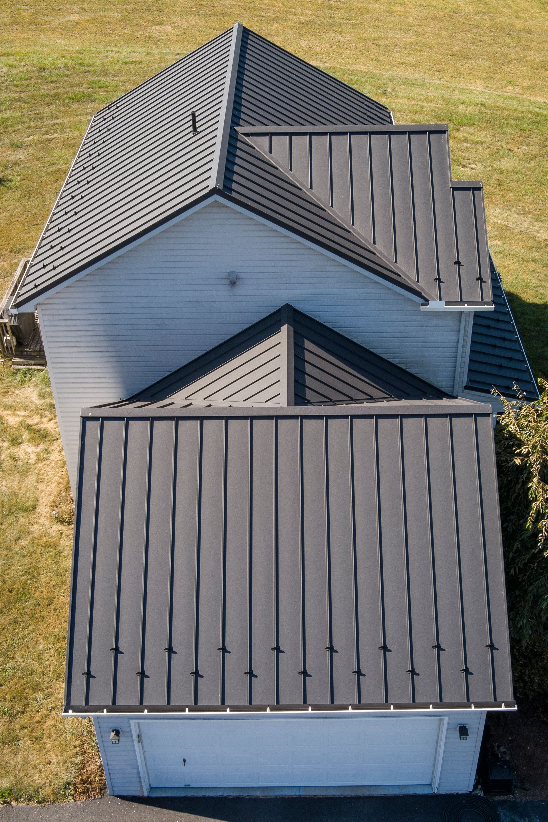 An aerial view of a white house with a dark metal roof and a detached garage featuring matching metal roofing.