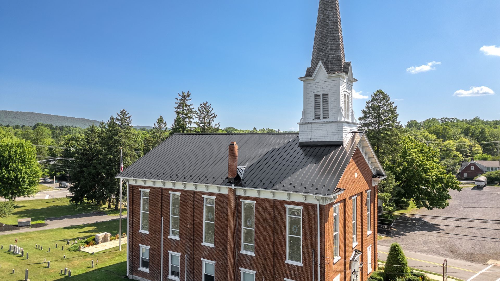 Brick church with white steeple against a blue sky; trees and graveyard in the background.