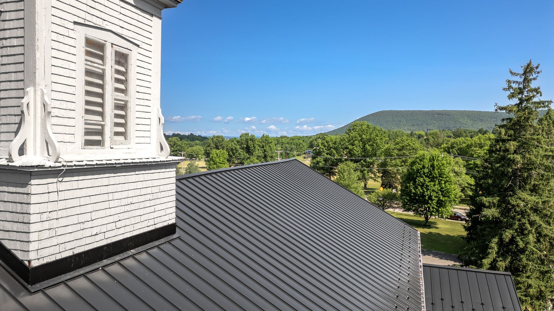View from a white building tower roof, overlooking a green landscape and blue sky.