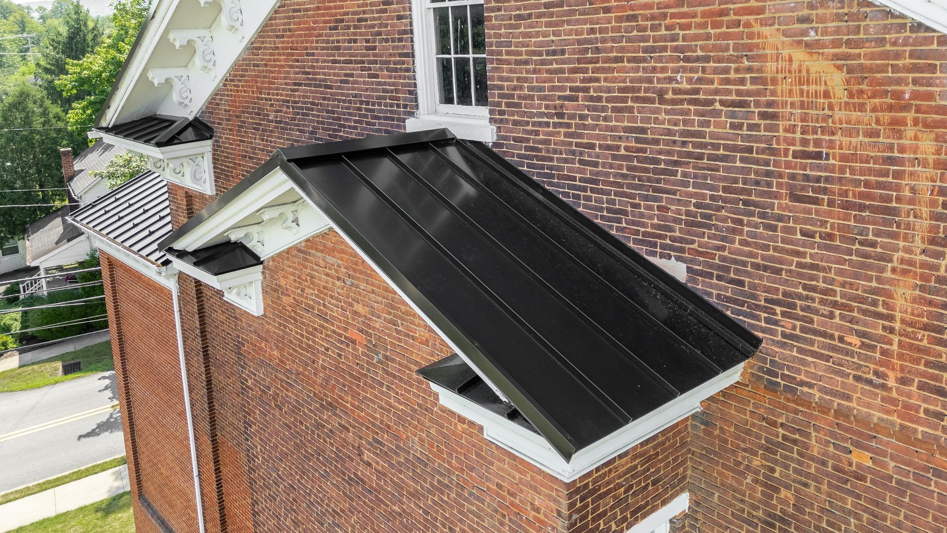 Black metal roof over a brick building, with white trim and a window.