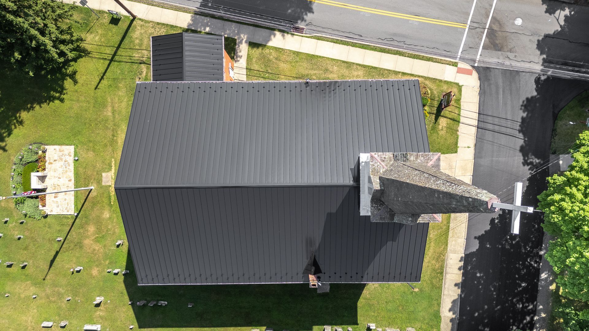 Overhead view of a church with a dark roof, a steeple, and a small cemetery beside it.