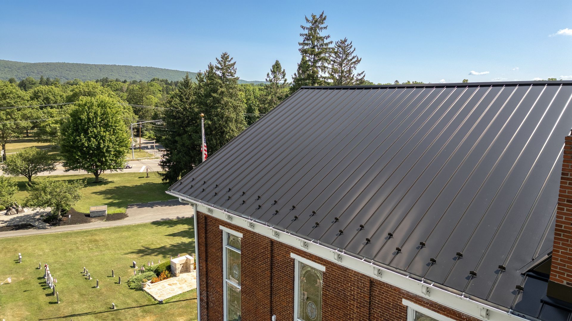 Black metal roof on a brick building with a view of a cemetery and trees.