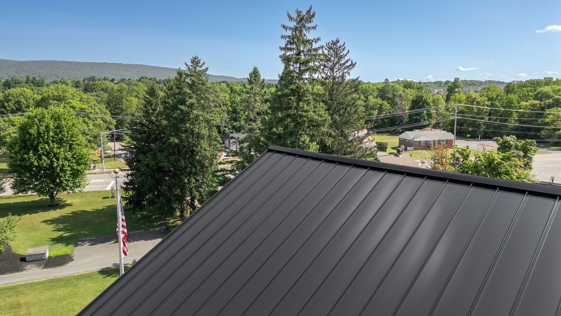 Black metal roof with a view of trees, buildings, and a mountain range under a blue sky.