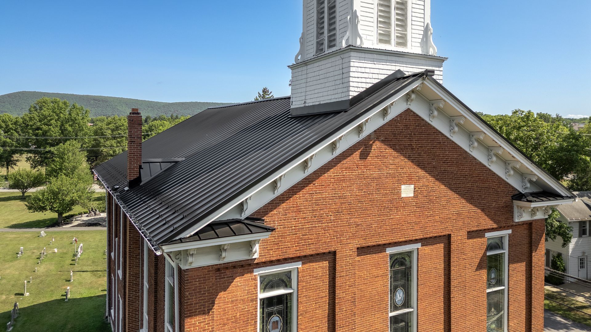 Brick church with black roof, white steeple, and windows, under a blue sky.