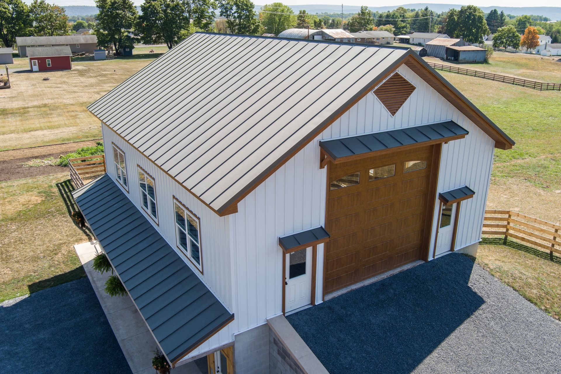 A white barn with a dark metal roof, large wooden garage door, and side porch, situated on a rural property.