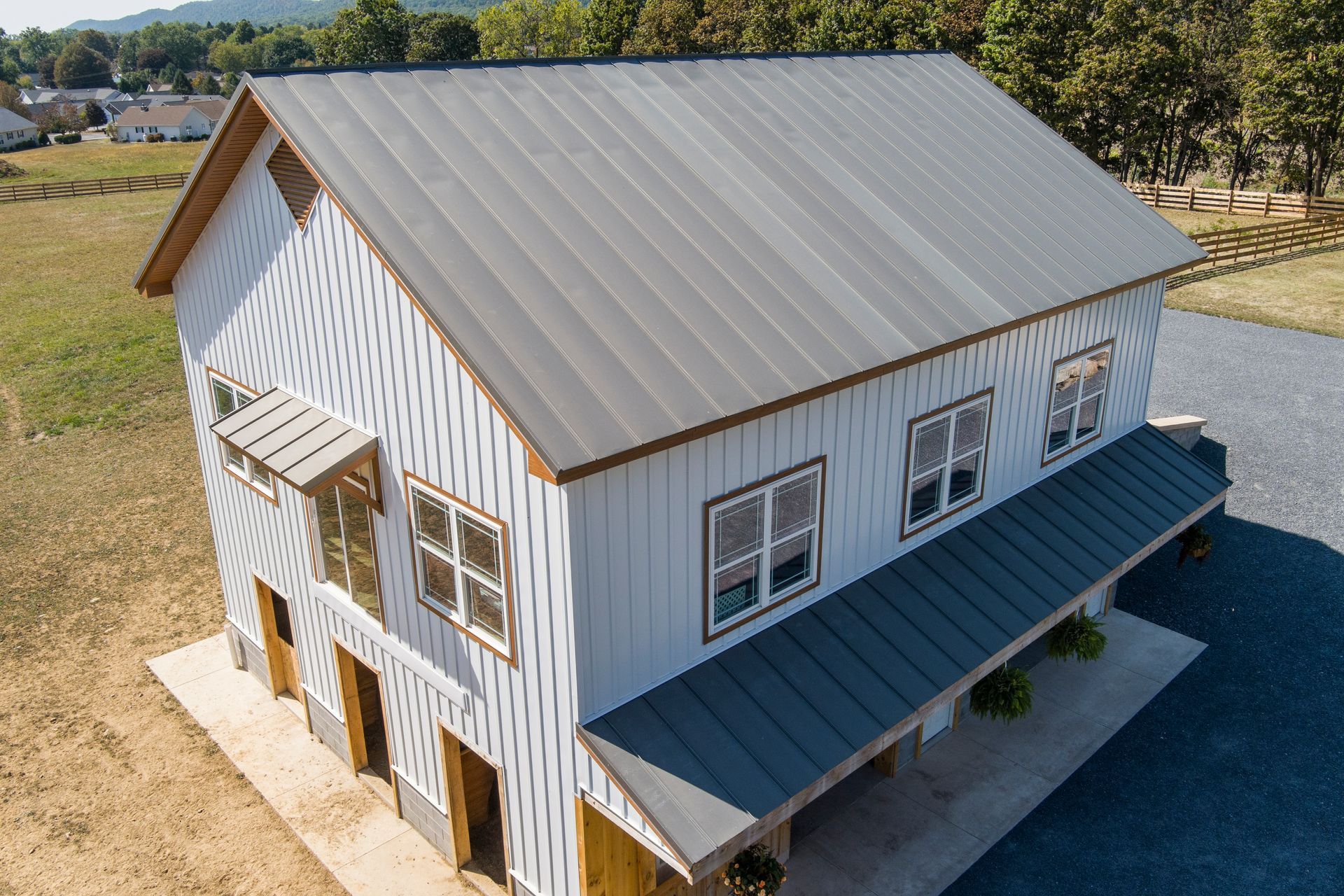 A two-story white barn with vertical siding and a dark gray metal roof, set in a sunny, grassy rural landscape.