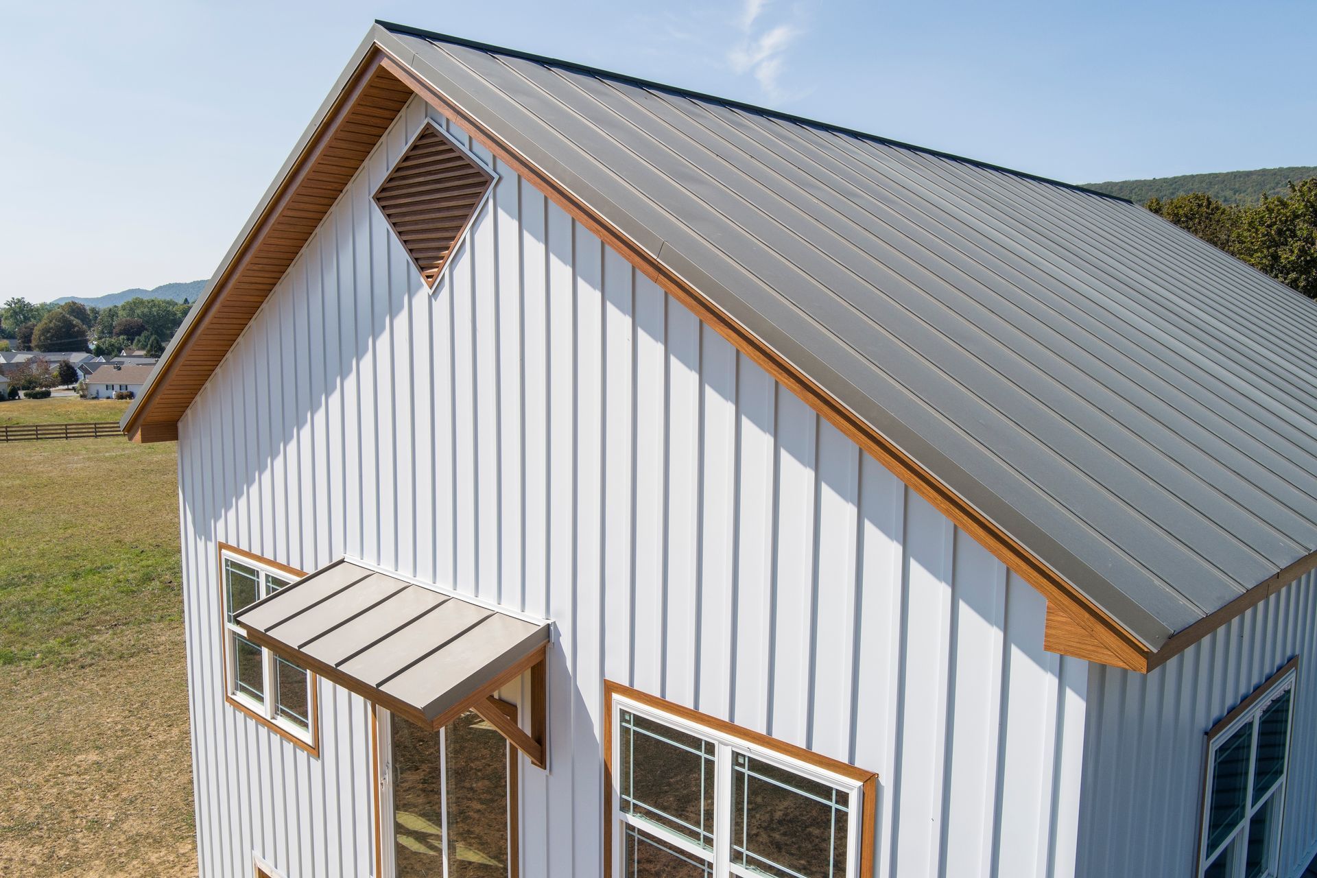A white shed with vertical metal siding, a grey metal roof, a diamond-shaped vent, and a small awning over the door.